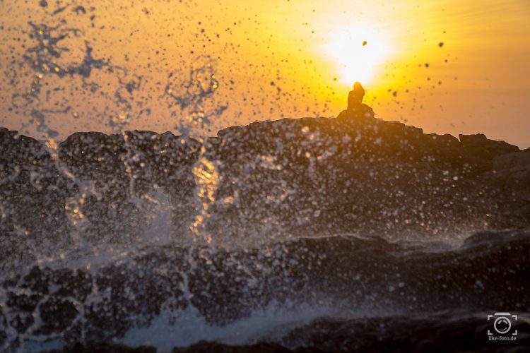 Reisefotografie Tipps - Frau im Sonnenuntergang am Meer mit Wasserspritzern